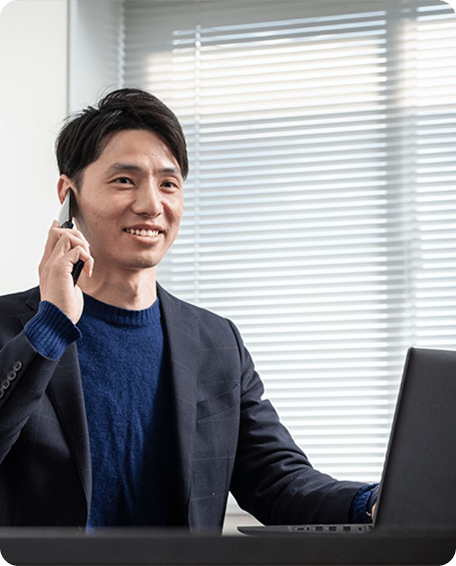 黒いジャケットを着た男性が、オフィスでスマートフォンを使って通話している様子