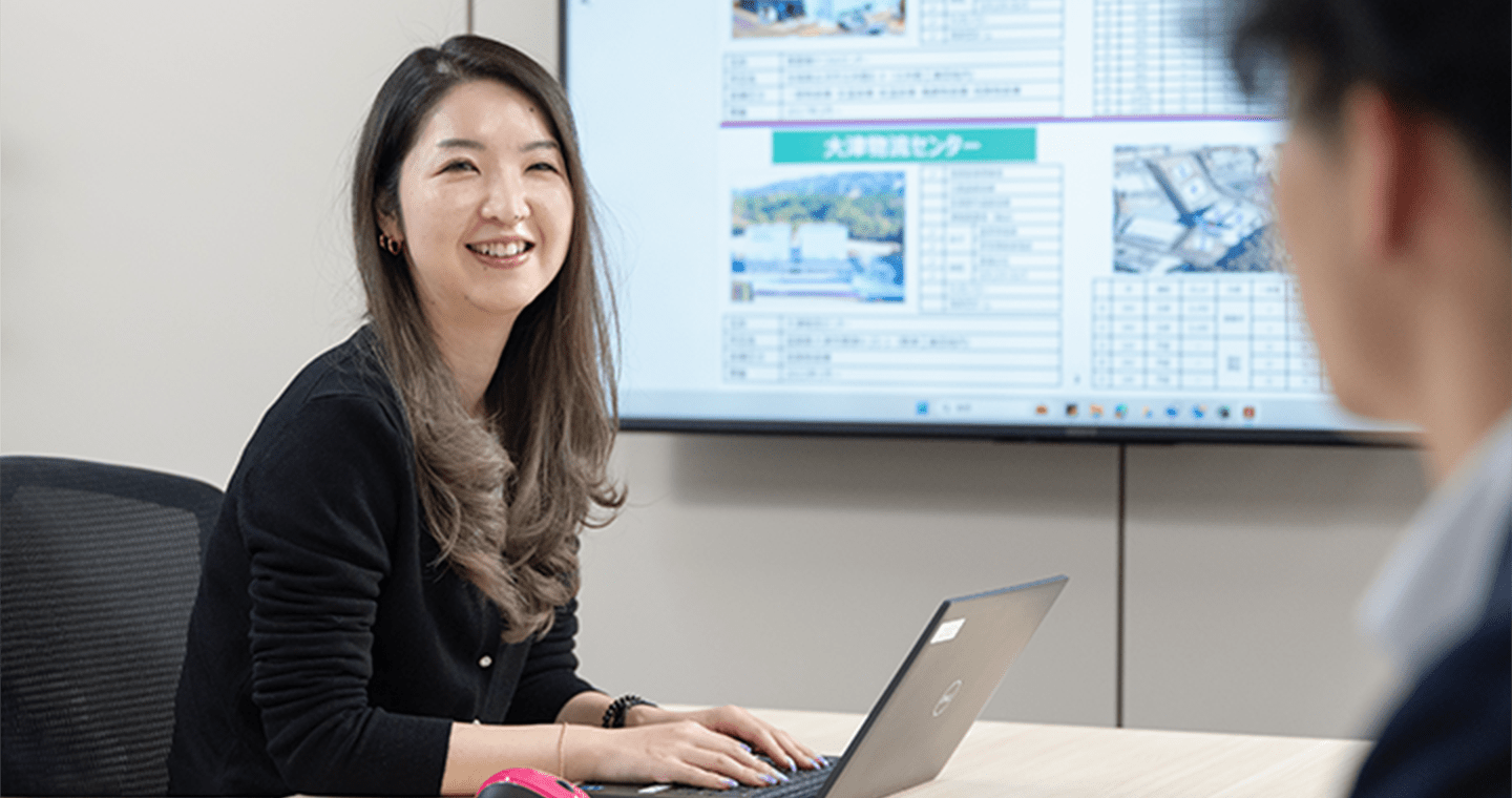 ノートパソコンを開いた女性が、会議室で同僚と打ち合わせをしている様子