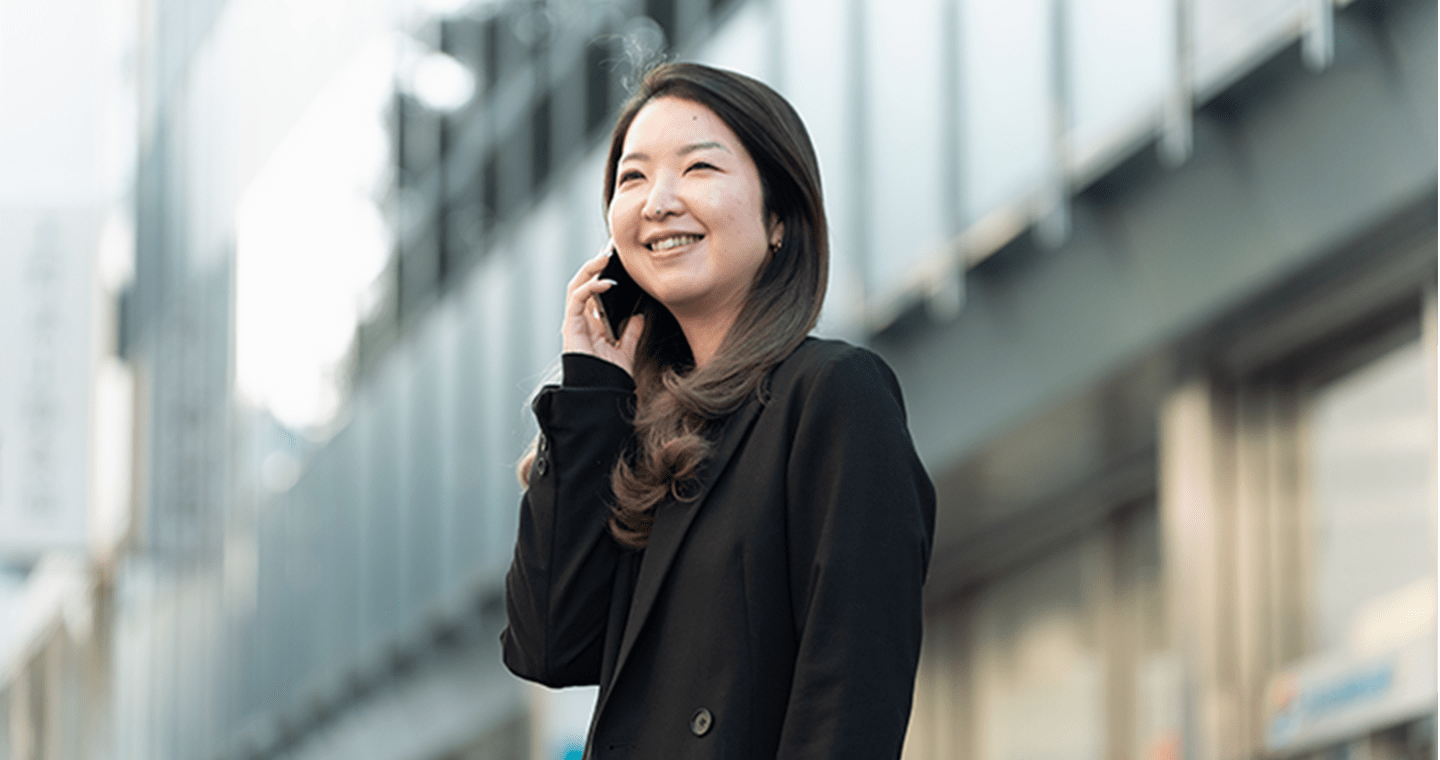 黒いジャケットを着た女性が、屋外でスマートフォンを使って通話している様子