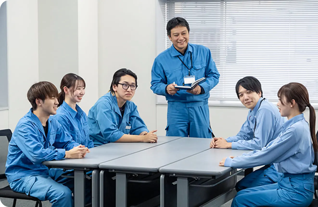 青い制服を着た6人の社員がテーブルを囲みにこやかに話し合いをしている様子